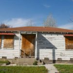 The front part and lawn of an abandoned house with boarded-up windows and door.